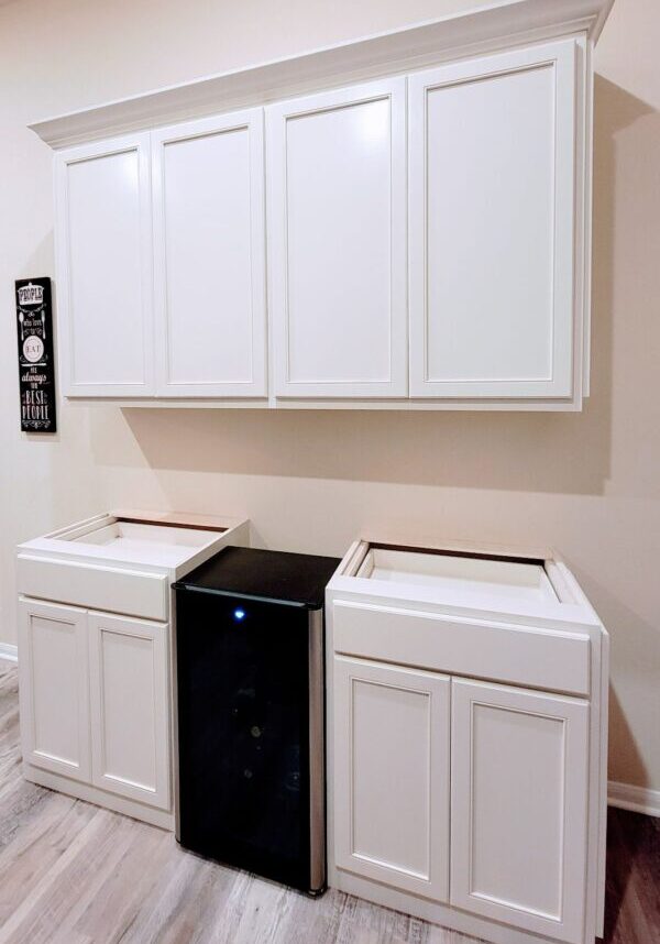 A kitchenette with white cabinets, a wine cooler, and a trash bin compartment features exceptional custom furnishing.