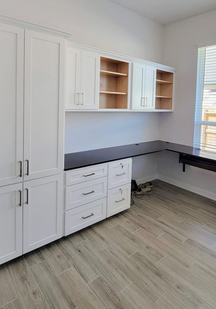 A modern home office with white cabinetry, built-in shelves, and an exceptional custom furnishing black desk area.