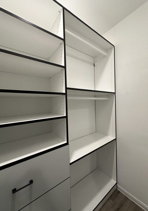 An empty, white modern bookshelf with black framing in a bright room, showcasing exceptional custom furnishing.