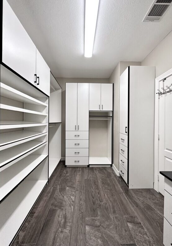 Modern walk-in closet with white cabinetry and built-in shelving, featuring a wood-style flooring.