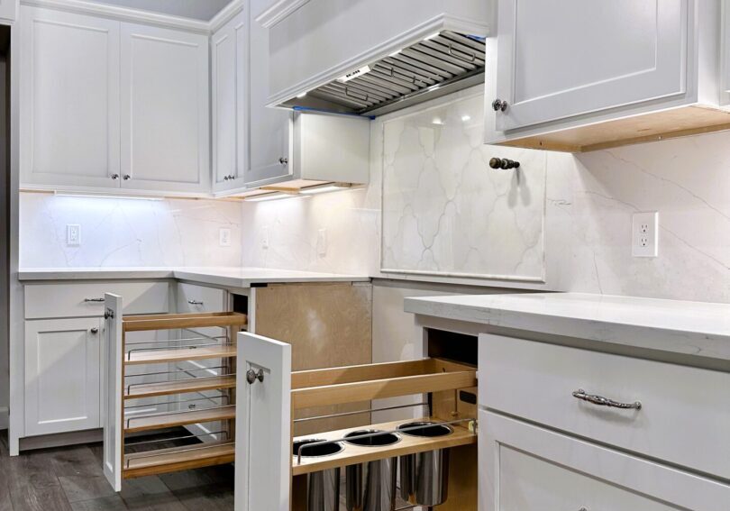A modern kitchen with white cabinets, stainless steel handles, exceptional custom furnishing, and pull-out storage solutions.