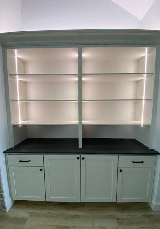 Built-in white bookshelf with cabinet base and exceptional custom furnishing led shelf lighting in a modern interior.